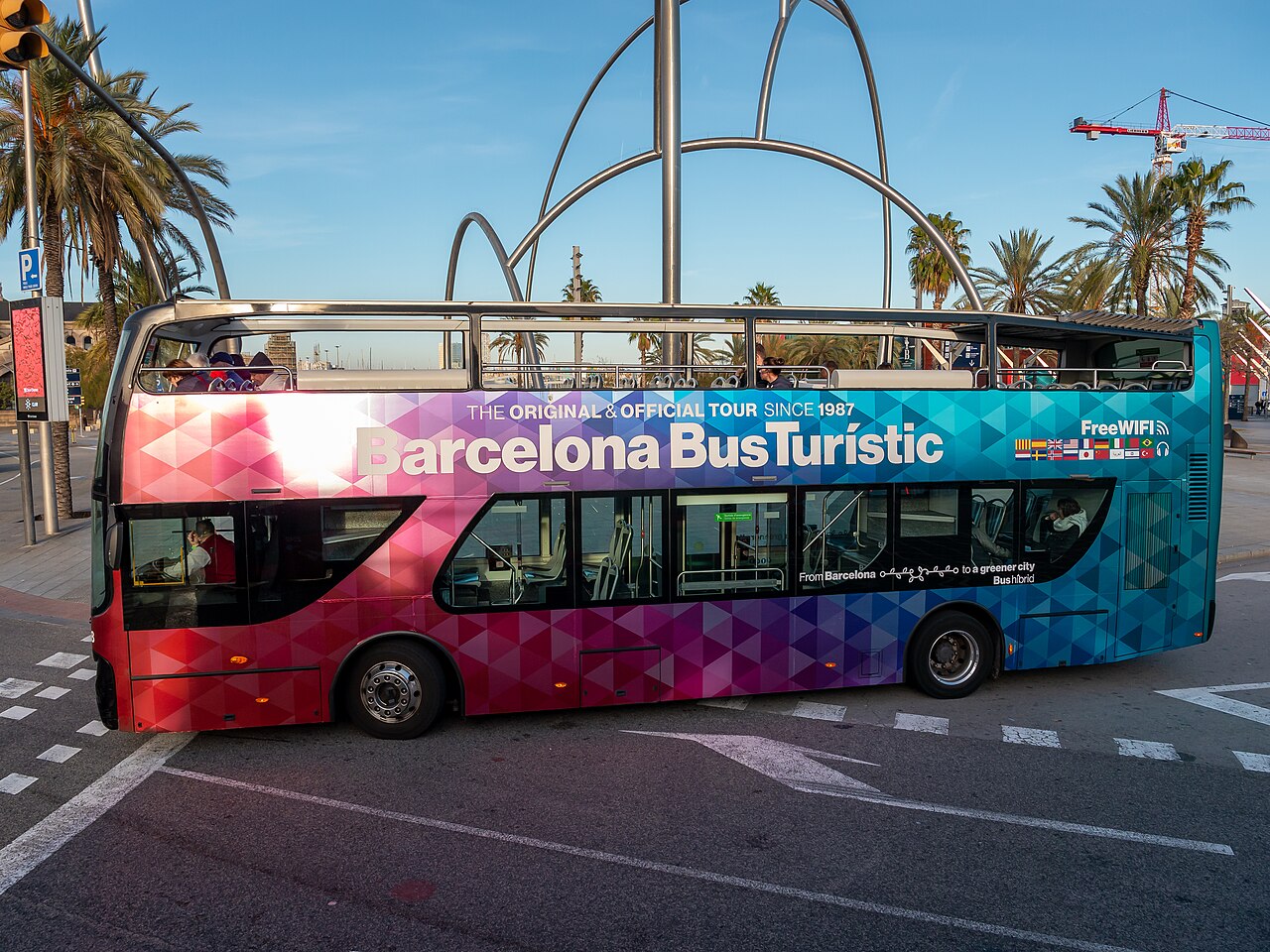 Ein offener Doppeldecker des Barcelona Bus Turístic an einer Straße mit Palmen in Barcelona