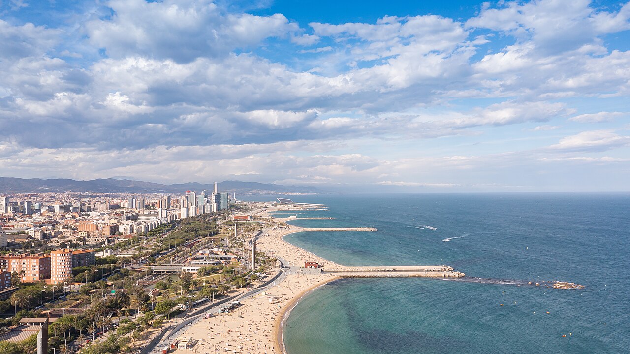 Luftaufnahme des Strands Nova Icària zwischen seinen Wellenbrechern, dahinter der Bogatell-Strand und die Hochhäuser von Diagonal Mar